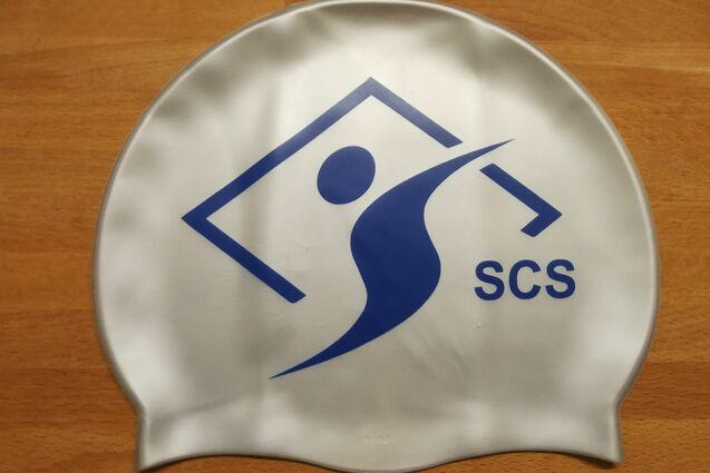 Schwimmkappe mit blauem Logo und Schriftzug "SCS" auf einer Holzoberfläche.