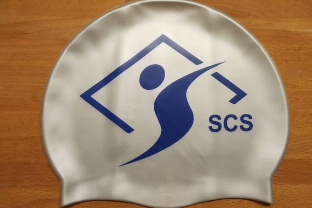 Schwimmkappe mit blauem Logo und Schriftzug "SCS" auf einer Holzoberfl&auml;che.