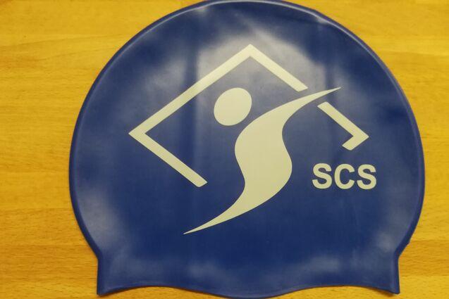 Blaues Schwimmhaube mit weißem Logo und der Aufschrift „SCS“ auf hellem Holzuntergrund.