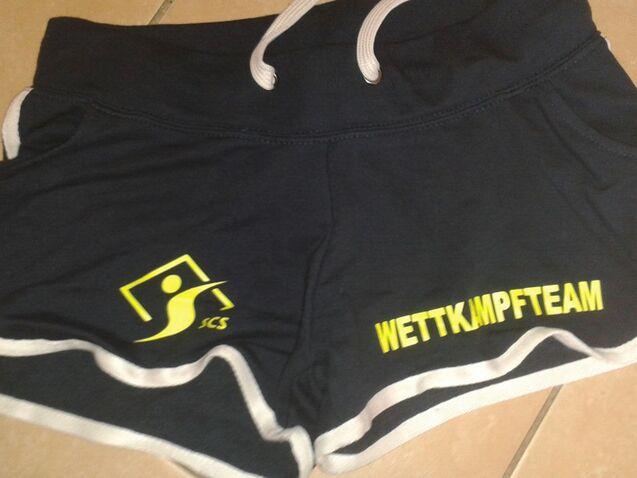 Dunkelblaue Sportshorts mit grauem Saum und dem Schriftzug &bdquo;WETTKAMPFTEAM&ldquo; in Gelb.