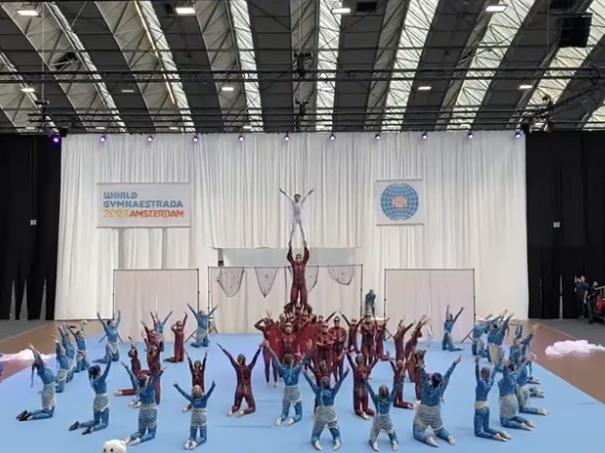 Gruppenspieler in bunten Kostümen führen eine akrobatische Darbietung auf einer Bühne während der World Gymnaestrada in Amsterdam vor.