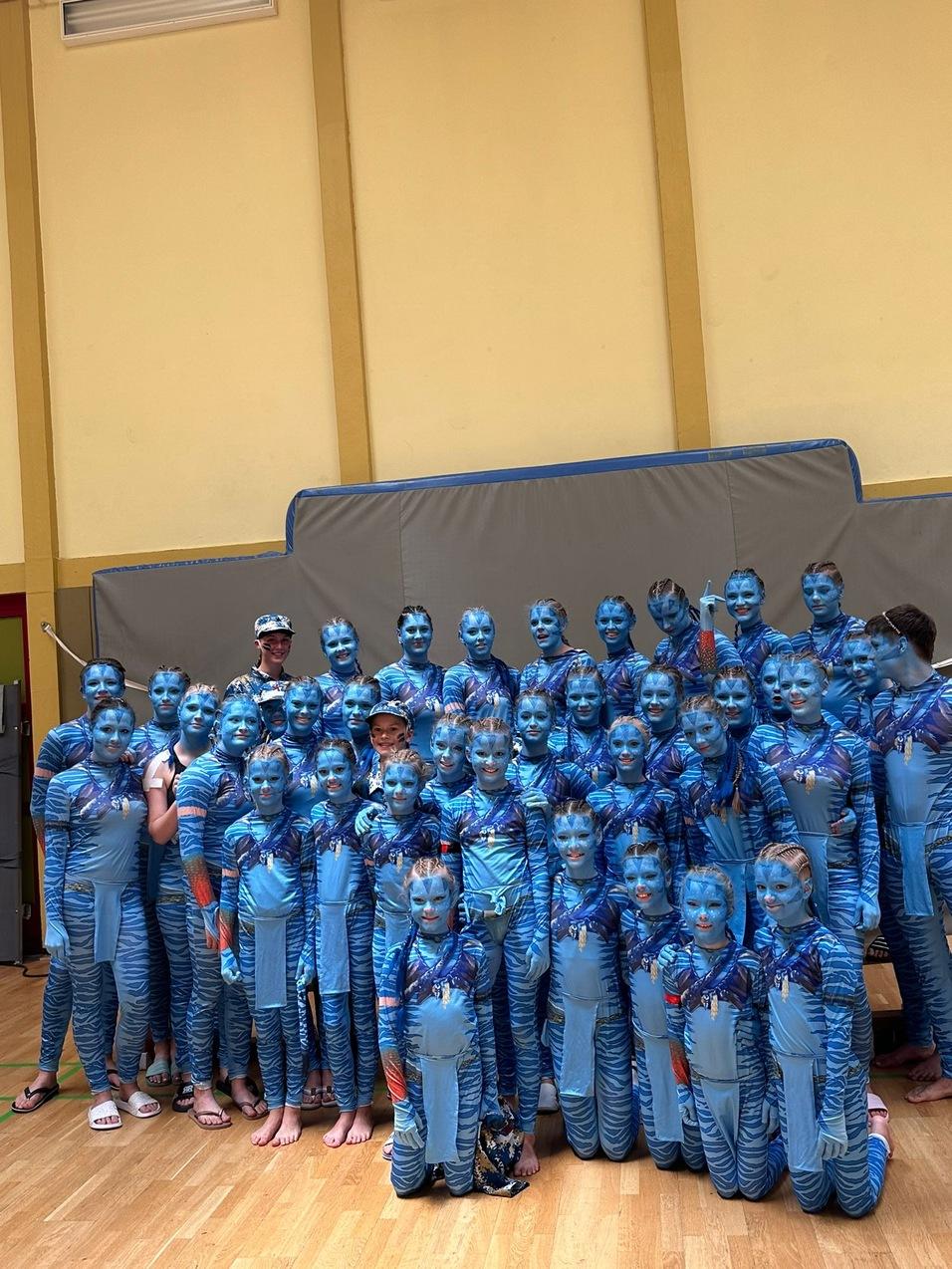Gruppenshot von Kindern in blauen Ganzkörperanzügen mit blau bemalten Gesichtern, stehen in einer Halle.