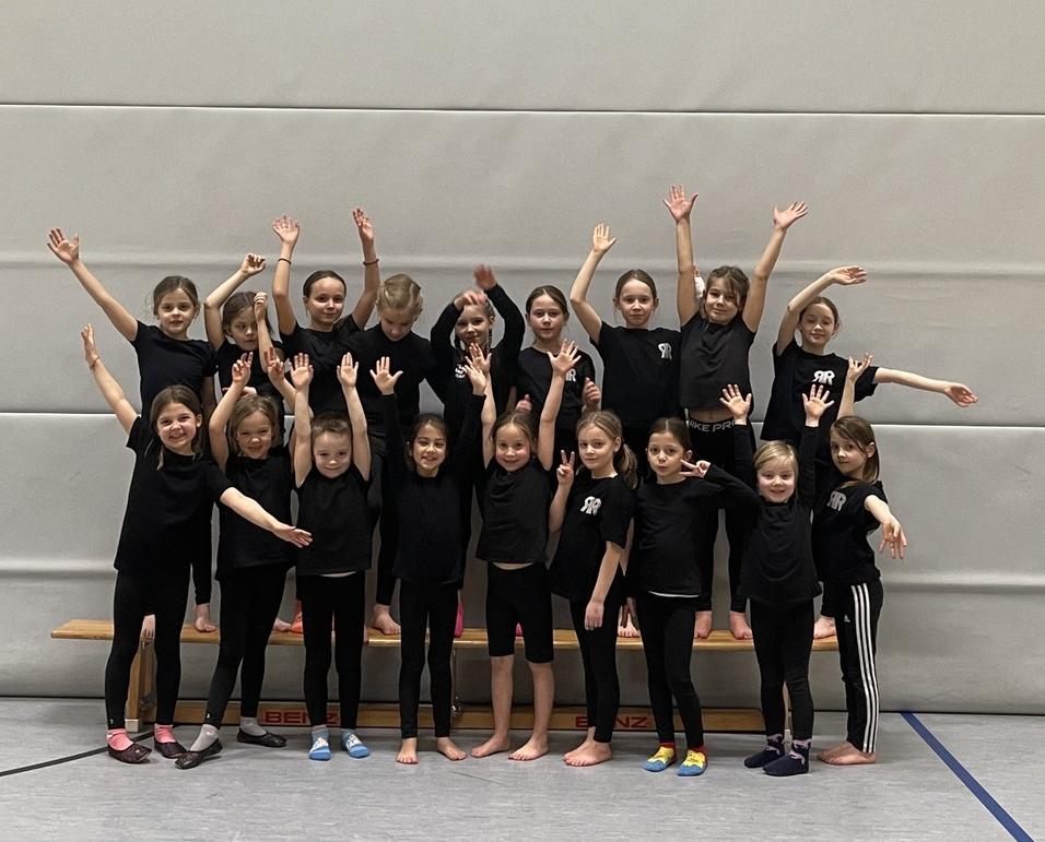 Gruppenfoto von Mädchen in schwarzen T-Shirts, die fröhlich auf einer Bank stehen und die Arme heben.