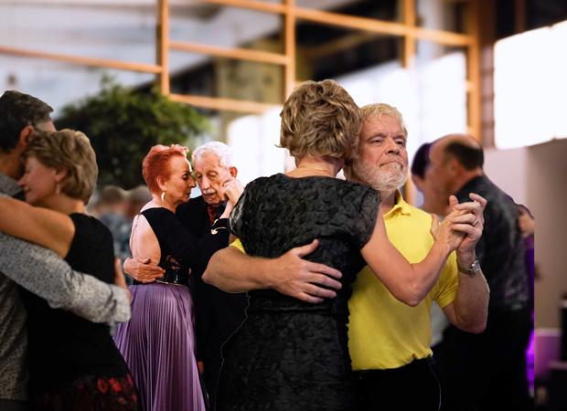 Tanzende Paare in einem festlichen Ambiente, Fokus auf ein Paar in enger Umarmung.