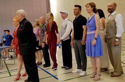 Gruppe von Menschen in eleganter Kleidung, bereit für eine Tanzaufführung, in einer Sporthalle.