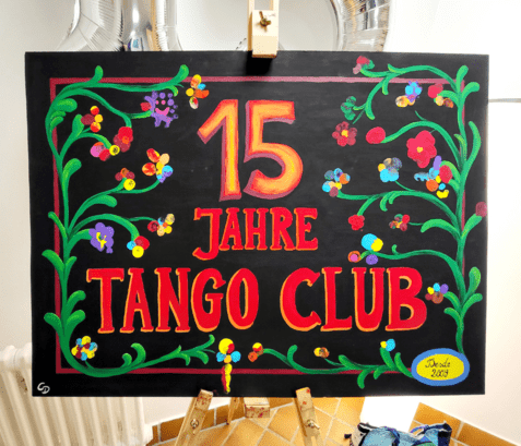 Bunte Tafel mit der Aufschrift „15 Jahre Tango Club“ umrahmt von floralen Motiven und einem Datum.