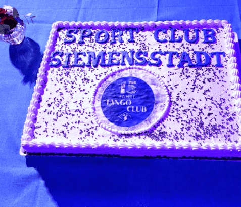 Torte mit Aufschrift „Sport Club Siemensstadt“ und „15 Jahre Tango Club“ auf blauer Tischdecke, mit Schokoladenstreuseln.