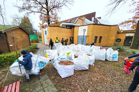 Gruppierung von weißen Säcken mit Laub im Freien, während Personen im Hintergrund einen Arbeitsdienst leisten.