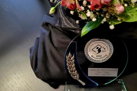 Trophäe des Sport Club Siemenstadt Berlin 2024 für Katja Fiebig, Trainerin des Jahres, mit Blumenarrangement.