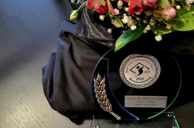 Trophäe des Sport Club Siemenstadt Berlin 2024 für Katja Fiebig, Trainerin des Jahres, mit Blumenarrangement.