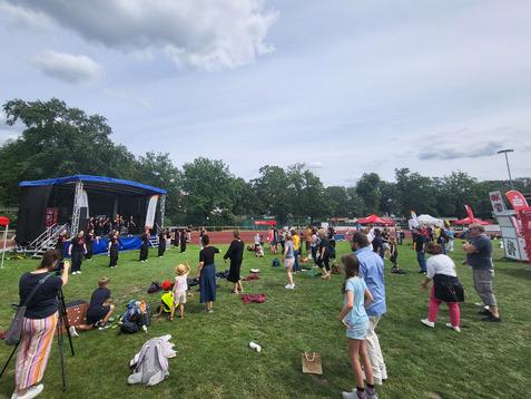 Menschenmenge vor einer Bühne im Freien, mit Performern auf der Bühne und Ständen im Hintergrund.