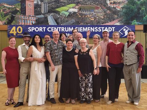 Gruppe von 15 Menschen in festlicher Kleidung, lächelnd auf einer Tanzfläche vor einem Banner mit dem Schriftzug „40 Jahre Sport Centrum Siemensstadt“.