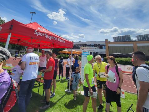 Gruppierung von Menschen am Infozelt der Sportjugend Berlin bei einem Laufevent, mit Teilnehmern in Sportkleidung.