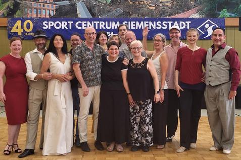 Gruppe von 15 Menschen in festlicher Kleidung, lächelnd auf einer Tanzfläche vor einem Banner mit dem Schriftzug „40 Jahre Sport Centrum Siemensstadt“.