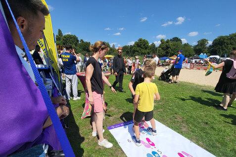 Familienfest im Freien mit Kindern, die auf einem Spielfeld mit bunten Zahlen stehen und eine Anleitung erhalten.