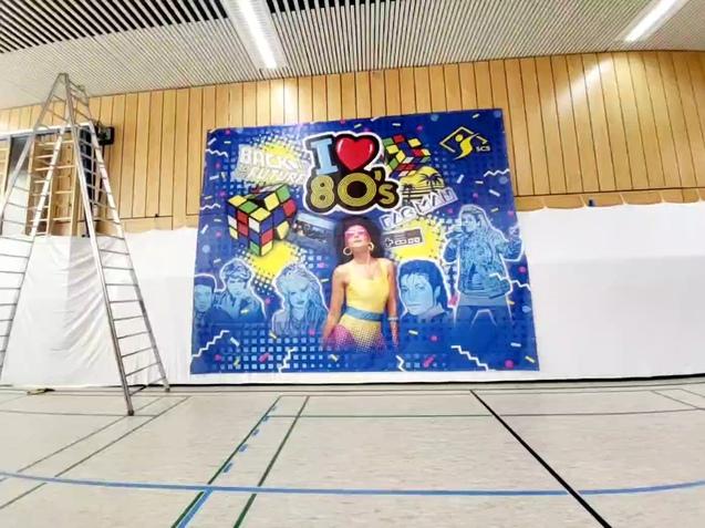 Großes buntes Wandbild mit 80er-Jahre-Motiven und einem Rubik's Cube in einer Sporthalle, neben einer Leiter.