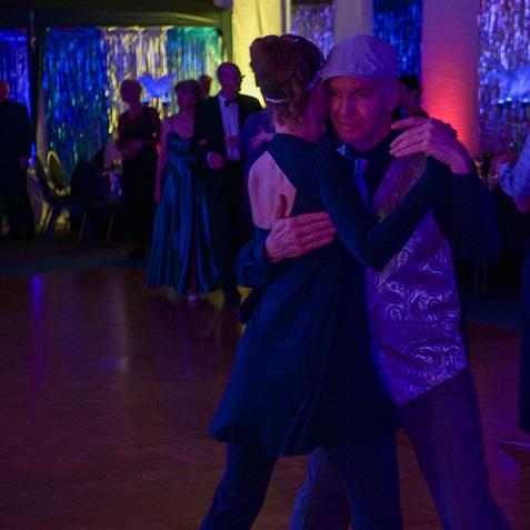 Tanzpaar in eleganter Kleidung bewegt sich harmonisch auf einer beleuchteten Tanzfläche während einer Veranstaltung.