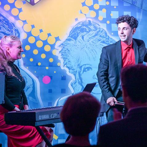 Musiker mit Kontrabass auf einer Bühne, im Hintergrund bunte Wand mit retro Motiven und Publikum.