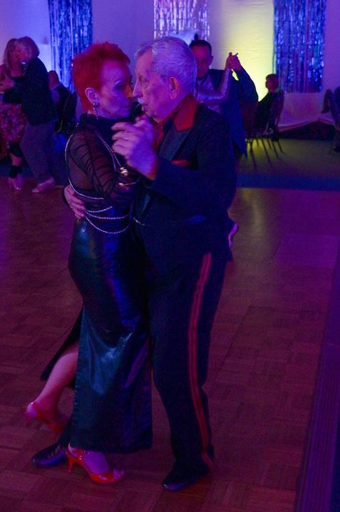 Tanzendes Paar in festlicher Kleidung unter bunten Lichtern auf einer Tanzfläche, mit Fokus auf ihre Körperhaltung.