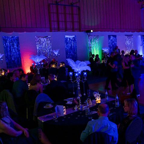 Festliche Tanzveranstaltung in einem beleuchteten Saal mit Tänzern und elegant gedeckten Tischen.