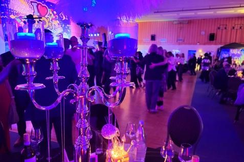 Elegante Tischdeko mit einem Kristallleuchter, farbigen Kerzen und tanzenden Gästen bei einer festlichen Veranstaltung.