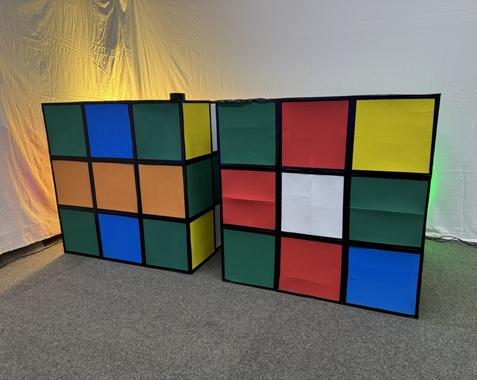 Zwei große, bunte Rubik's Cube-Wände in Orange, Blau, Grün, Rot, Weiß und Gelb auf einem grauen Teppich.