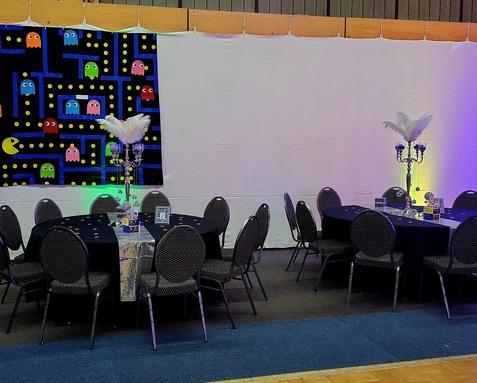 Festlich gedeckte Tische mit schwarzen Tischdecken und Kerzenleuchtern, im Hintergrund ein Pac-Man-Themenbanner.