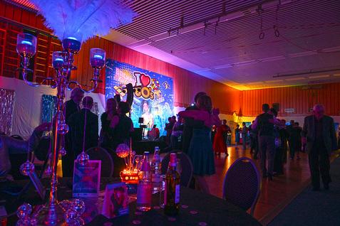 Beleuchteter Veranstaltungsraum mit tanzenden Gästen und festlicher Dekoration im Stil der 80er Jahre.