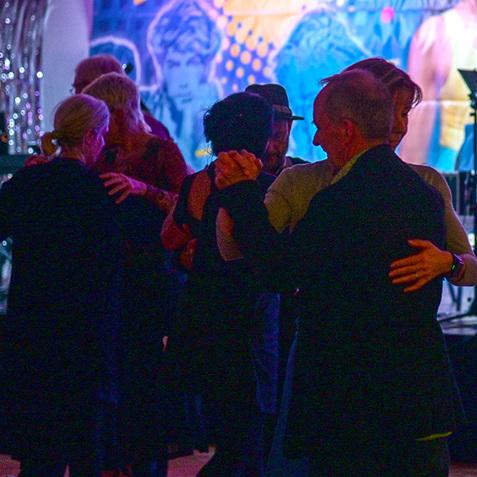 Tanzende Menschen vor einer bunten Wanddekoration in festlicher Atmosphäre mit Beleuchtung.