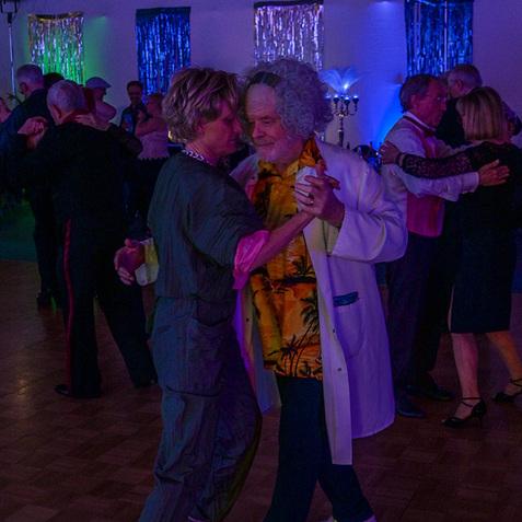 Tanzende Paare in festlicher Kleidung bei einem Event mit bunten Lichtern und festlicher Dekoration im Hintergrund.