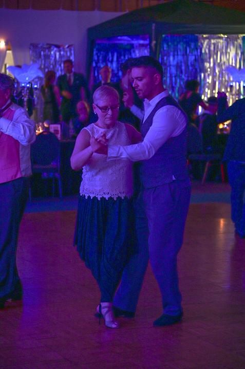 Tanzpaar in formeller Kleidung, das eng umschlungen auf einer beleuchteten Tanzfläche tanzt.