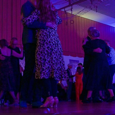 Tanzende Paare in eleganter Kleidung unter buntem Licht in einem Veranstaltungsraum.