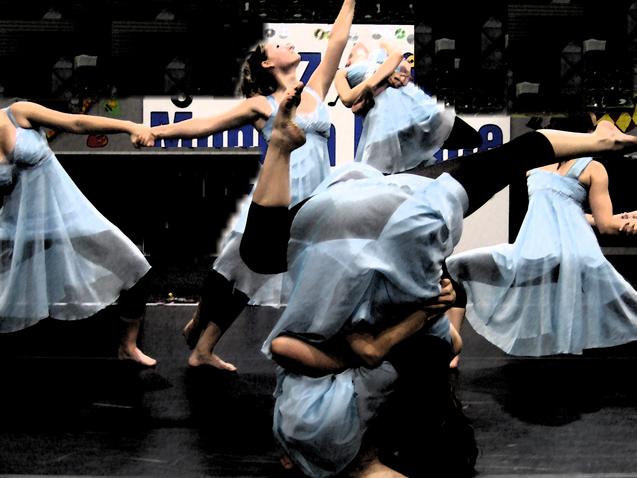 Sechs T&auml;nzerinnen in blauen Kleidern f&uuml;hren eine koordinierte Choreografie auf einer B&uuml;hne aus.