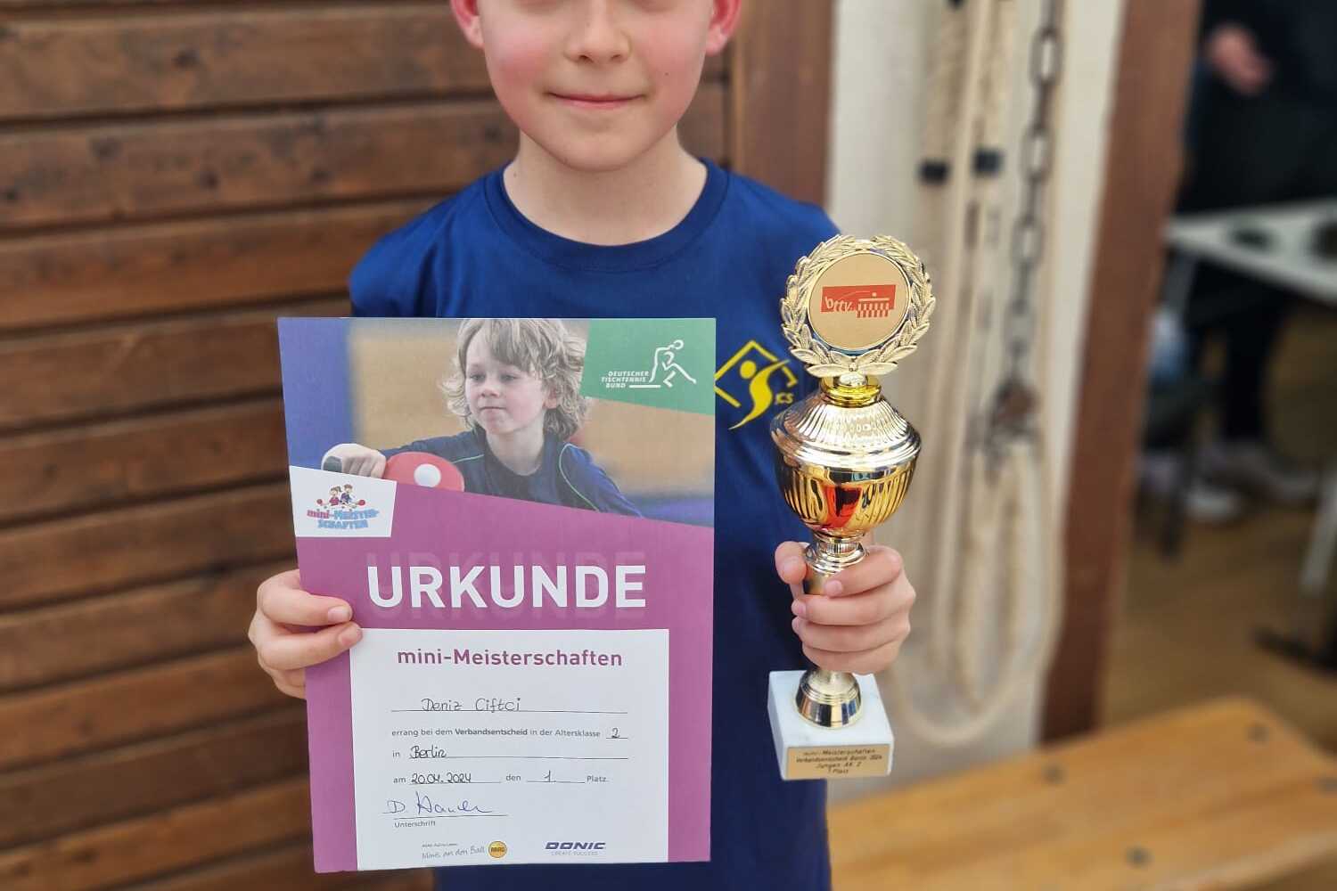 Ein Junge hält eine Urkunde und einen Pokal nach den mini-Meisterschaften in einer Innenraumumgebung.