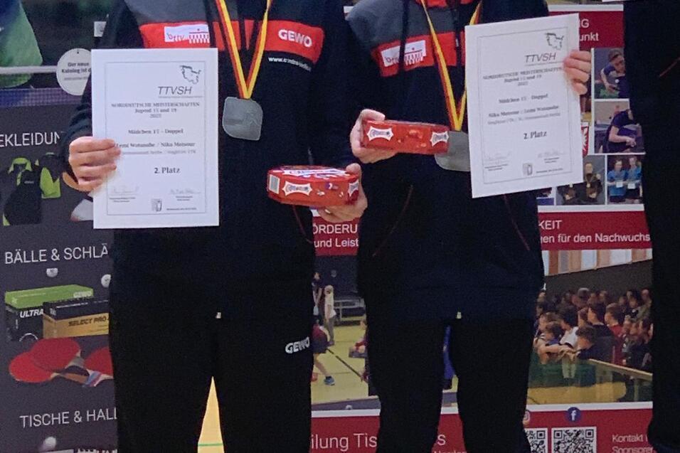 Zwei M&auml;dchen stehen auf dem Siegertreppchen und halten Urkunden f&uuml;r den 1. und 2. Platz in einem Tischtennisturnier.