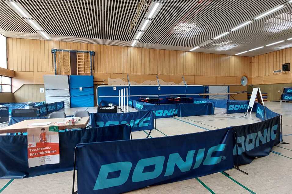 Tischtennis-Turnierhalle mit mehreren Tischen, Wettkampfzubeh&ouml;r und einer Informatiionsstelle, markiert mit DONIC-Bannern.