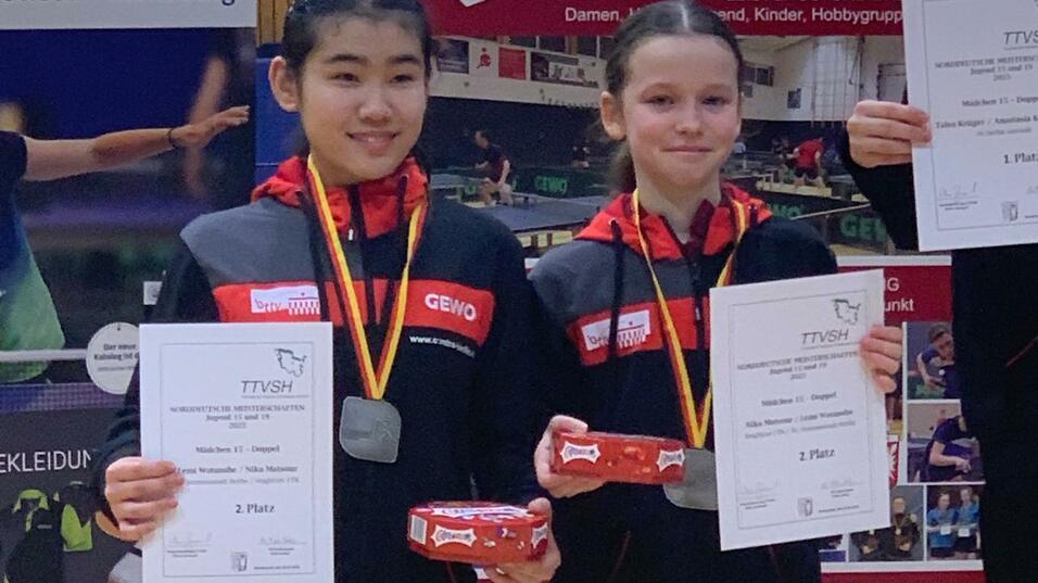 Zwei Mädchen stehen auf dem Siegertreppchen und halten Urkunden für den 1. und 2. Platz in einem Tischtennisturnier.