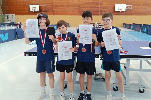 Vier Kinder halten Urkunden und Medaillen nach dem Tischtennisturnier in einer Sporthalle.