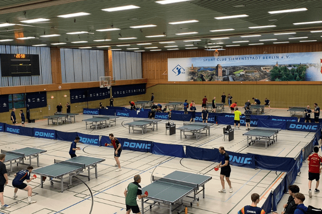 Vielzahl von Tischtennisplatzen in einer Sporthalle, Spieler trainieren und nutzen Ausr&uuml;stung in einer lebhaften Atmosph&auml;re.