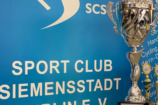 Vereinspokal des Sport Clubs Siemensstadt Berlin e.V. vor einer blauen Wand mit dem Vereinslogo und Text.
