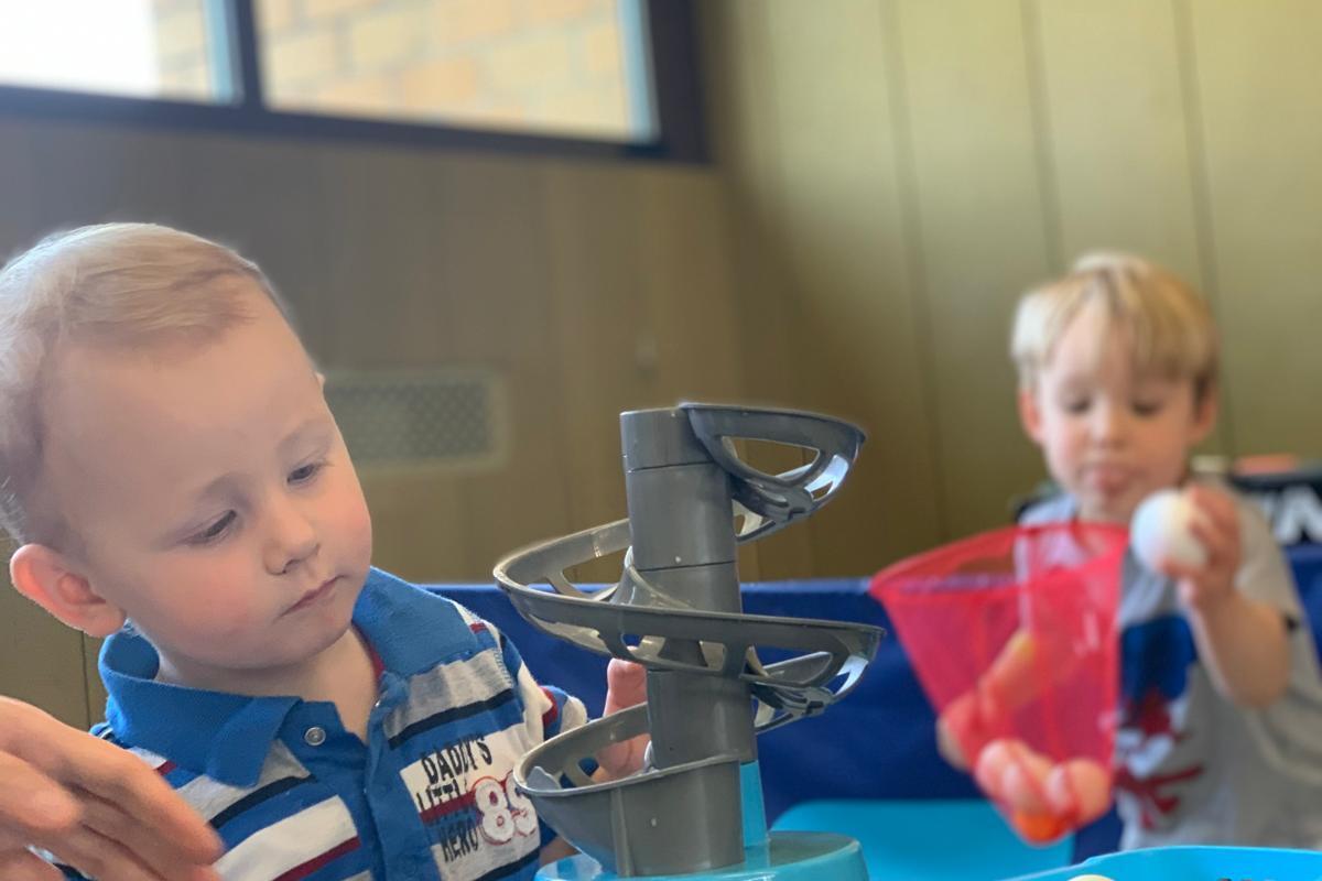 Zwei kleine Kinder spielen mit einem Spielger&auml;t, das Tischtennisb&auml;lle durch eine spiralf&ouml;rmige Bahn rollt.