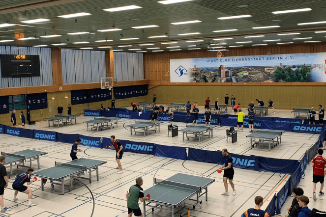 Vielzahl von Tischtennisplatzen in einer Sporthalle, Spieler trainieren und nutzen Ausr&uuml;stung in einer lebhaften Atmosph&auml;re.
