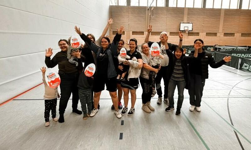 Gruppe von Personen mit erhobenen Händen in einer Sporthalle, fröhliche Stimmung, einige halten Spielzeug in der Hand.