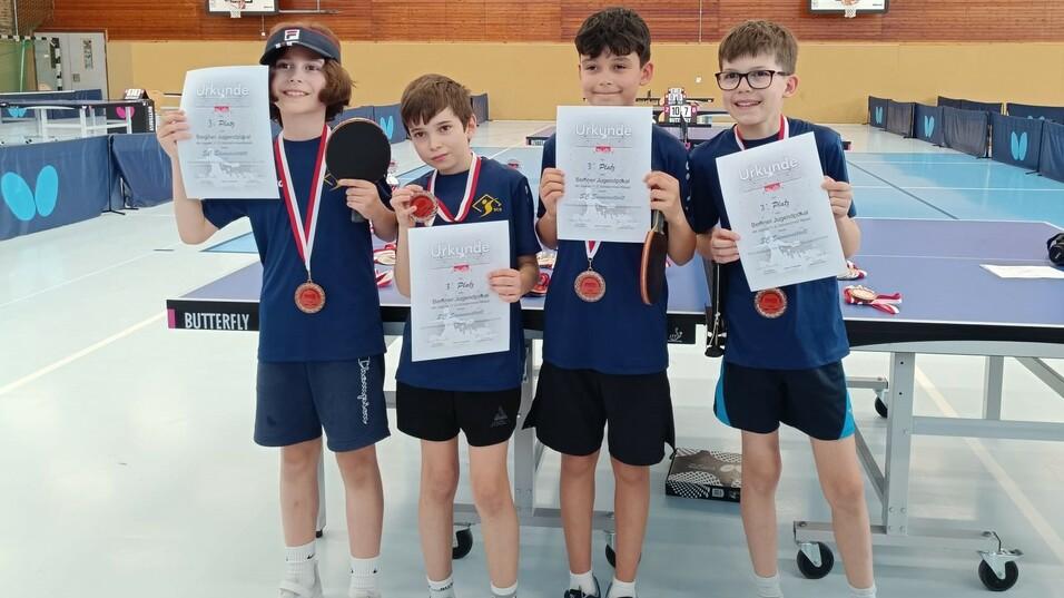 Vier Kinder halten Urkunden und Medaillen nach dem Tischtennisturnier in einer Sporthalle.