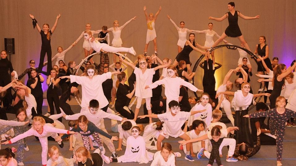 Große Gruppe von Kindern und Jugendlichen in Kostümen mit Gesichtsbemalung, die an einer Tanzaufführung teilnehmen.