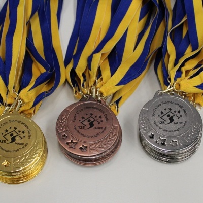 Drei Medaillen in Gold, Silber und Bronze mit blauen und gelben B&auml;ndern, beschriftet mit &bdquo;125 Jahre&ldquo;.