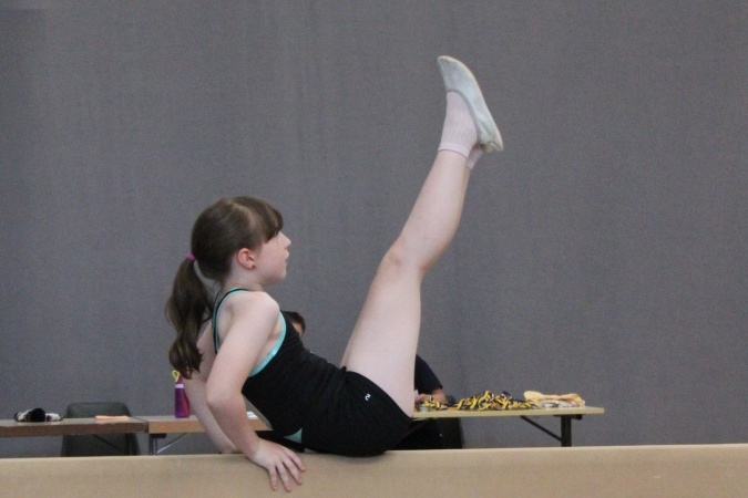 M&auml;dchen in Sportkleidung balanciert auf einem Schwebebalken und hebt ein Bein hoch.