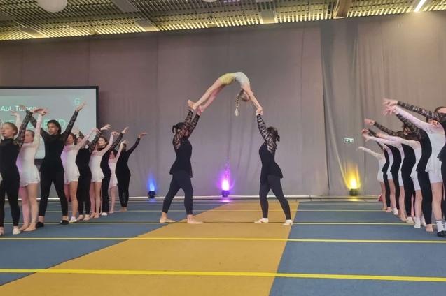 T&auml;nzerinnen in Sportkleidung f&uuml;hren eine Hebefigur auf einer B&uuml;hne w&auml;hrend einer Auff&uuml;hrung aus.