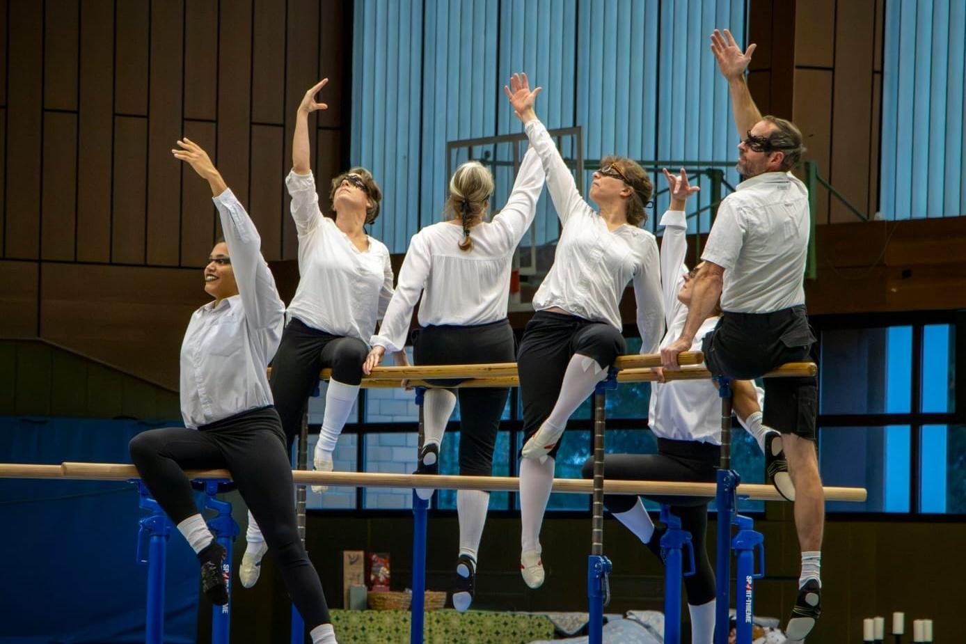 Sechs Turner in wei&szlig;en Hemden &uuml;ben Kunstturnen an Parallelbarren in einem Sportzentrum.