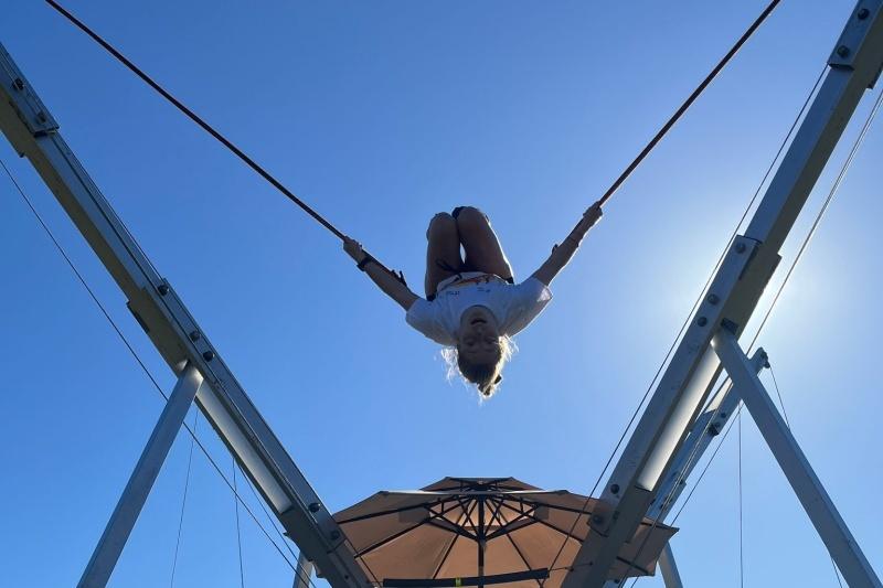 M&auml;dchen schwingt kopf&uuml;ber an einem Seil unter blauem Himmel &uuml;ber einem Sonnenschirm.